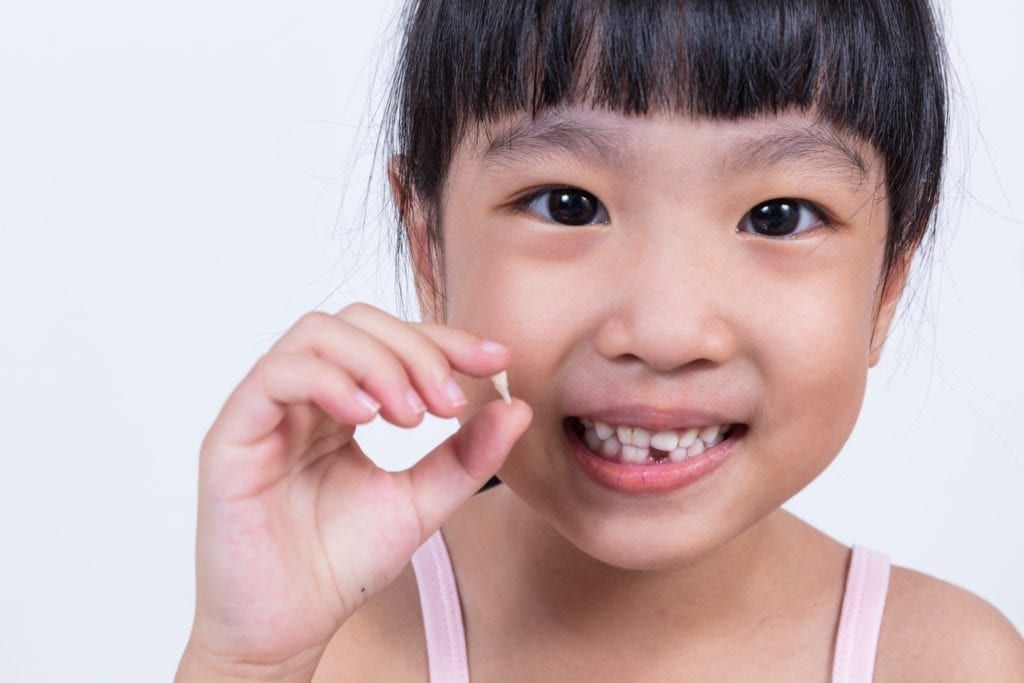 young girl holding tooth she pulled out