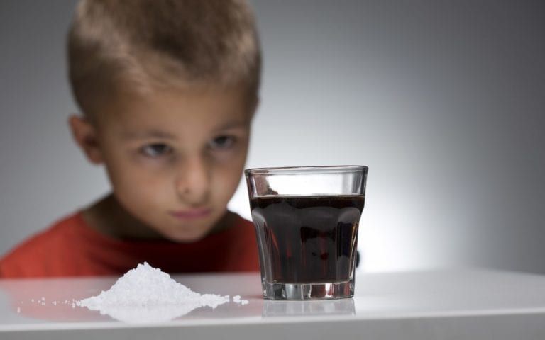 Child looking at glass of soda next to pile of sugar