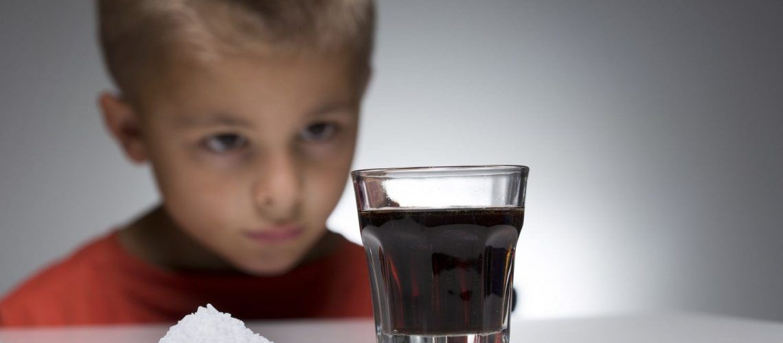 Child looking at glass of soda next to pile of sugar