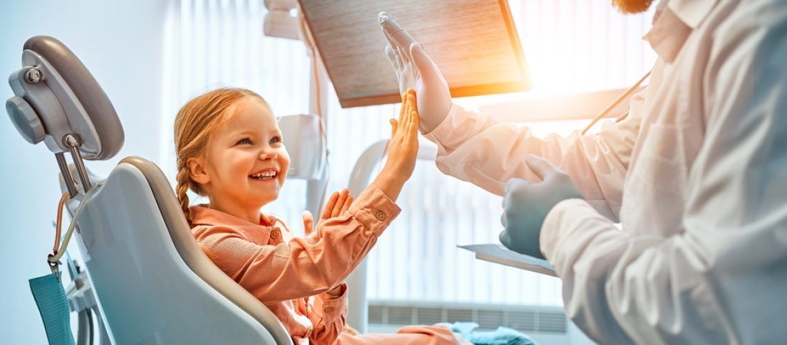 A,Little,Girl,Is,Sitting,In,A,Dentist's,Chair,,Giving